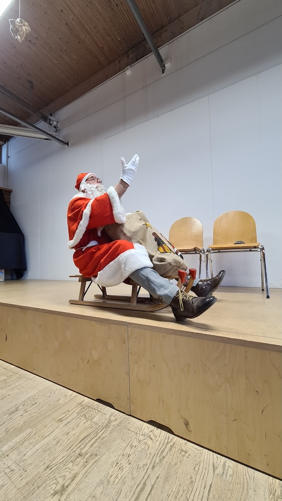 Theaterstück: Ein Nikolaus sitzt auf dem Schlitten, seine Hand mit weissem Handschuh ist hoch gehoben